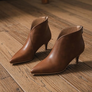 May include: A pair of brown leather ankle boots with a pointed toe and a low heel. The boots have a V-shaped opening at the top and a zipper at the back. The heels are approximately 2 inches high.