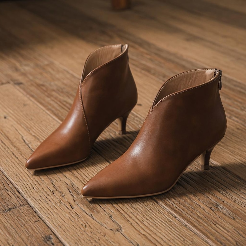 May include: A pair of brown leather ankle boots with a pointed toe and a low heel. The boots have a V-shaped opening at the top and a zipper at the back. The heels are approximately 2 inches high.