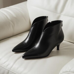 May include: A pair of black leather ankle boots with a pointed toe and a low heel. The boots have a V-shaped cut on the front and a zipper on the back. The boots are sitting on a white surface.