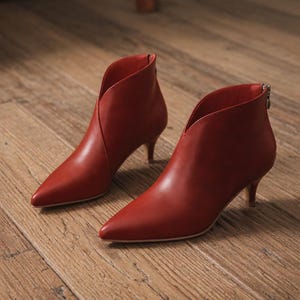 May include: A pair of red ankle boots with pointed toes and a low heel. The boots have a V-shaped cut at the ankle and a zipper at the back. The boots are made of a smooth, leather-like material.