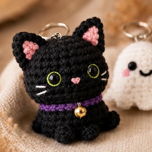 May include: A black crocheted cat keychain with pink inner ears, large black eyes with green outlines, a small pink nose, white embroidered whiskers, and a purple collar featuring a small gold-colored metal bell attached to a silver keyring.