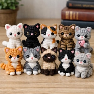 Può includere: Una collezione di undici figurine di gatti all'uncinetto in vari colori e motivi. I gatti hanno grandi occhi espressivi e sono disposti su una superficie di legno. Ogni gatto ha segni unici, tra cui strisce tabby, macchie calico e colori pieni.