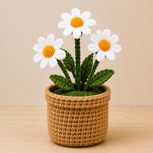 May include: A crocheted daisy plant in a brown pot. The daisies have white petals and yellow centres. The green leaves and stems contrast with the flowers. The pot is a light brown colour.