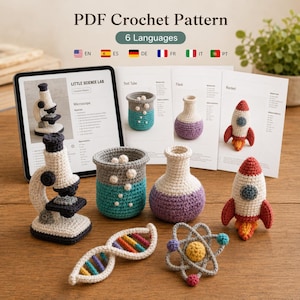 May include: A PDF crochet pattern for a science lab set featuring a microscope, test tube, flask, rocket, DNA strand, and atom. The set includes six languages and displays images of the finished crocheted items alongside printed instruction pages.