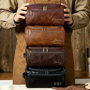 Puede incluir: Cuatro neceseres personalizados en tonos marrón y negro están apilados. Cada bolsa tiene una cremallera en la parte superior y un asa. La bolsa superior es marrón con el nombre "Thomas" grabado. La segunda bolsa es marrón con el nombre "Oliver" y un gráfico de montaña. La tercera bolsa es marrón oscuro con el nombre "Michael". La bolsa inferior es negra con las iniciales "KBT".
