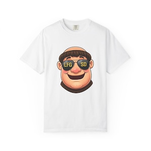 Puede incluir: Camiseta blanca con una ilustración de dibujos animados de una cara sonriente con gafas de sol. Las gafas de sol muestran el texto "LFG SD" en amarillo. La cara tiene pelo castaño y un cuello marrón.