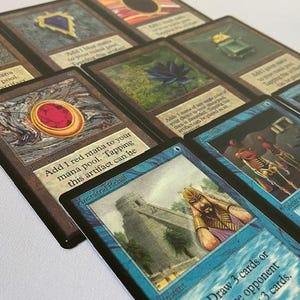 May include: A selection of Magic: The Gathering trading cards. The cards display diverse artwork and text, including a red gem artifact and the text "Add 1 red mana to your mana pool."
