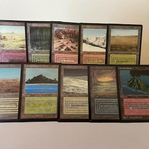 Könnte beinhalten: Eine Sammlung von zehn Magic: The Gathering Dual-Land-Karten, die in zwei Reihen angeordnet sind. Die Karten zeigen verschiedene Landschaftsillustrationen wie Wüsten, Wälder, Berge und eine Vulkaninsel, jeweils mit farbigen Rändern und Text.