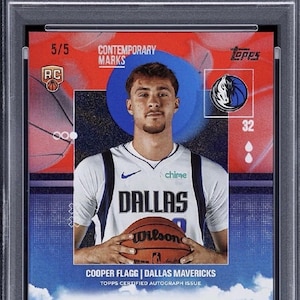 May include: A Cooper Flagg basketball card from the 2025 Topps set. The card features a photo of the player in a Dallas Mavericks jersey, holding a Wilson basketball. The card is graded GEM MT 10 by PSA and includes an autograph.