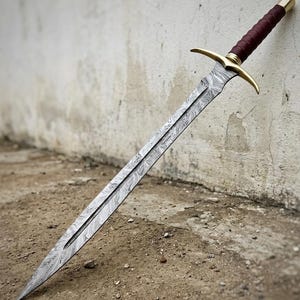 Può includere: Una lunga spada ornata con una lama a motivi, una guardia dorata e un'impugnatura avvolta in pelle bordeaux. La spada è appoggiata a un muro strutturato bianco sporco, mostrando la sua dettagliata lavorazione artigianale.
