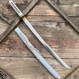 May include: A katana sword with a silver blade and white handle, featuring a gold-colored handguard. The scabbard is light blue with a decorative woven design. The sword rests on a wooden surface.