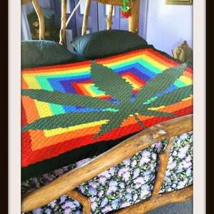 Könnte beinhalten: Eine Regenbogen-Häkeldecke mit einem grünen Marihuana-Blatt-Design. Die Decke liegt auf einem Holzbettgestell mit einer floral gemusterten Matratze. Der Text "www.CrochetCouch.com" und "getestet von Donna Ritenour" ist im Bild sichtbar.