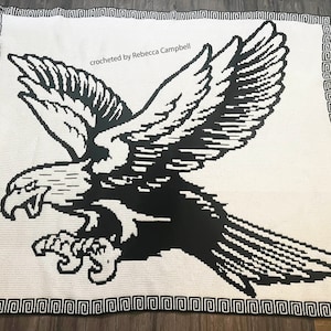 Op de afbeelding: Zwart-witte gehaakte deken met een gestileerd adelaarontwerp. De deken heeft een Grieks sleutelrand en de tekst "crocheted by Rebecca Campbell".