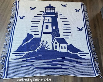 May include: A rectangular crochet blanket featuring a white background with a large blue lighthouse design, a small house, rocky terrain, and flying birds. The blanket has a blue and white striped border and fringe on the left and right sides.
