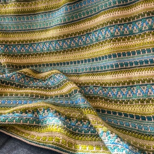 Puede incluir: Un afgan de punto de crochet a rayas verdes, azules y beige con el texto "Just a Yarn Sampler Afghan crocheted by Katharina Kohler" en la parte inferior.