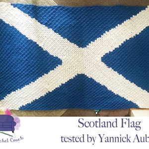 Op de afbeelding: Een gehaakt deken in de kleuren van de Schotse vlag. Het deken is blauw met een wit diagonaal kruis. De tekst "Scotland Flag tested by Yannick Aubin" staat onder het deken.