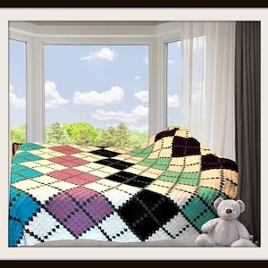Op de afbeelding: Een gehaakte deken met een veelkleurig argyle-patroon in tinten zwart, wit, taling, roze en paars, vergezeld door een kleine, lichtbruine pluche teddybeer die in de rechterbenedenhoek van het frame op het oppervlak zit.