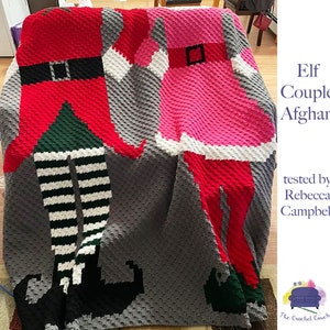 May include: A crochet blanket featuring a couple of elves, one in red and green and the other in pink and white. The blanket is made with a textured stitch and has a gray background. The text "Elf Couple Afghan" is visible in the image.