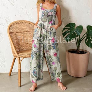 May include: A sleeveless jumpsuit featuring a light-coloured base with a botanical print of green leaves and vibrant pink flowers. The garment has a square neckline, wide-leg trousers, and side pockets. The text The Style Slate is overlaid on the image.