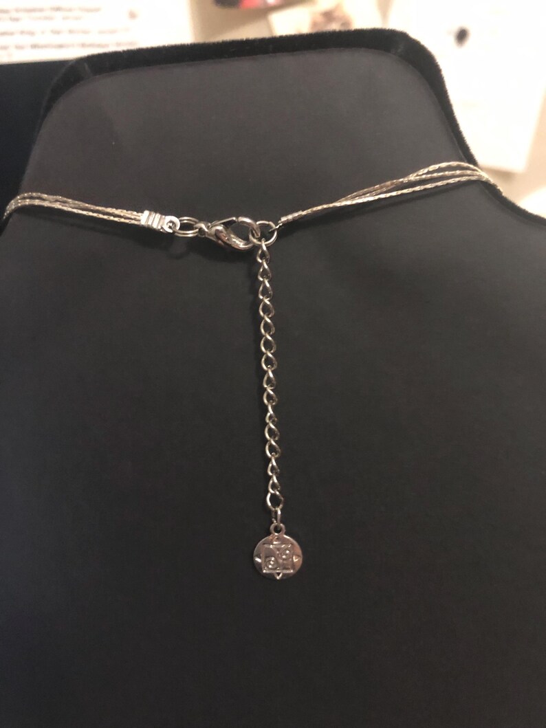 Puede incluir: Collar plateado con m&uacute;ltiples hilos finos, un cierre de mosquet&oacute;n y una cadena ajustable. El collar se exhibe en un maniqu&iacute; negro. Un peque&ntilde;o dije redondo cuelga al final de la cadena.