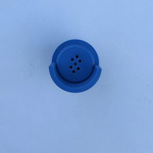 May include: A vibrant blue bottle stopper with a unique design. The stopper features a circular top with six small holes and a curved base. The object is set against a light blue background.
