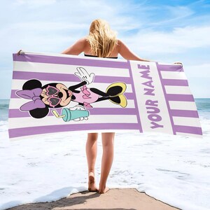 Pode incluir: Uma toalha de praia retangular com um padr&atilde;o de riscas verticais roxo-claras e brancas. A toalha apresenta um gr&aacute;fico da Minnie Mouse com &oacute;culos de sol em forma de cora&ccedil;&atilde;o e a segurar uma bebida azul-clara, com o texto YOUR NAME impresso.