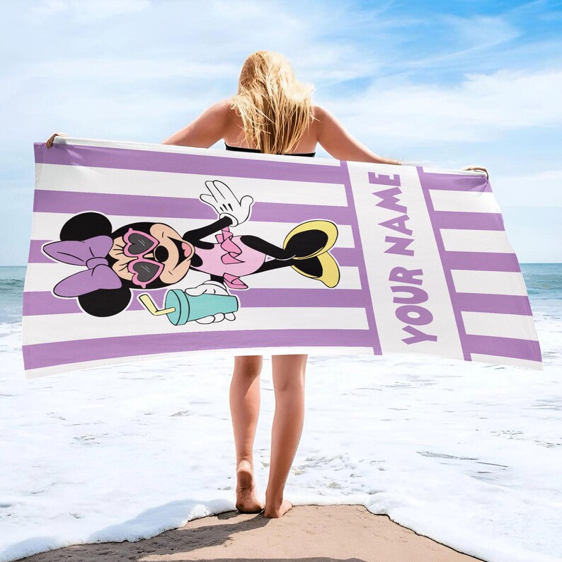 Pode incluir: Uma toalha de praia retangular com um padr&atilde;o de riscas verticais roxo-claras e brancas. A toalha apresenta um gr&aacute;fico da Minnie Mouse com &oacute;culos de sol em forma de cora&ccedil;&atilde;o e a segurar uma bebida azul-clara, com o texto YOUR NAME impresso.