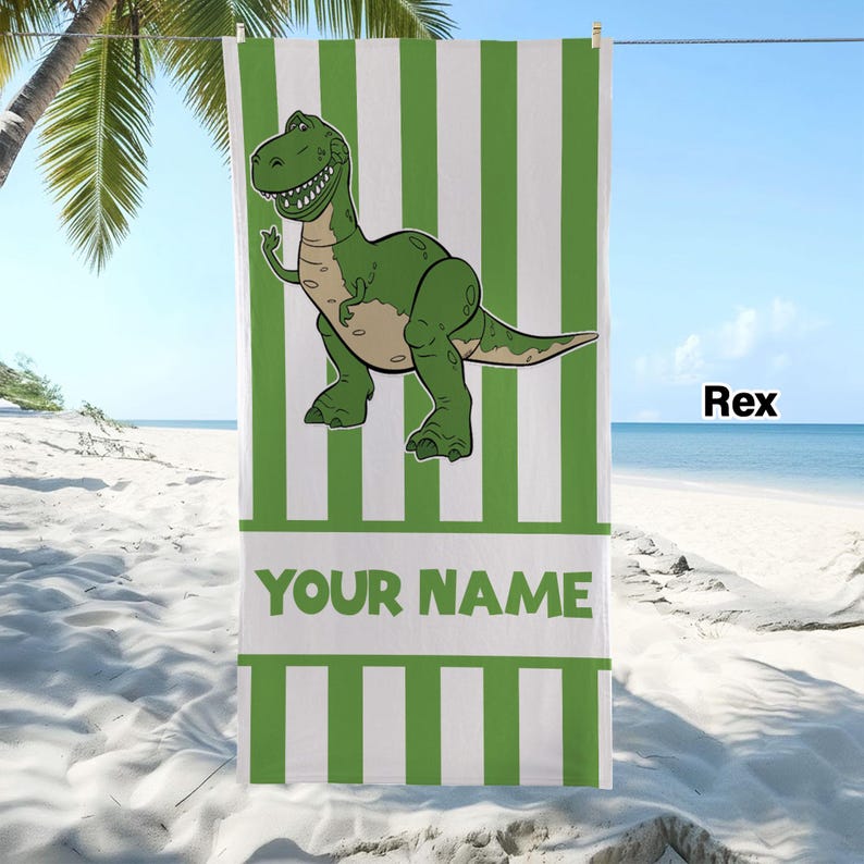 May include: A rectangular beach towel featuring vertical green and white stripes. A green cartoon dinosaur is centred in the upper portion. Below the dinosaur, a white horizontal band contains the green text YOUR NAME in capital letters.