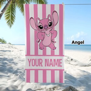 May include: A rectangular beach towel featuring a pink and white vertical striped pattern. The center displays a cartoon character named Angel with large ears and a pink body. Below the character is a white horizontal band with the text YOUR NAME.