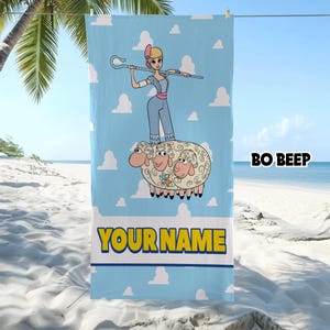 Puede incluir: Una toalla de playa rectangular de color azul claro con una ilustraci&oacute;n de dibujos animados de Bo Peep sosteniendo un cayado de pastor mientras est&aacute; de pie sobre tres ovejas. El fondo tiene nubes blancas. El texto BO BEEP y YOUR NAME est&aacute; impreso.