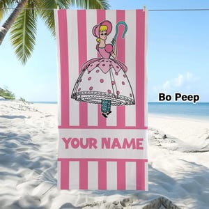 May include: A rectangular beach towel featuring a pink and white vertical striped pattern. The centre displays a cartoon illustration of a character wearing a bonnet and a polka-dot dress, holding a blue shepherd's crook. The text YOUR NAME is printed.