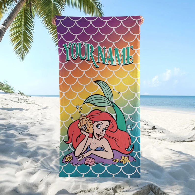 K&ouml;nnte beinhalten: Ein rechteckiges Strandtuch mit einem lebendigen Regenbogen-Farbverlauf und einem wiederkehrenden Meerjungfrauenschuppen-Muster. Der Text "YOUR NAME" ist in gro&szlig;en t&uuml;rkisfarbenen Buchstaben oben &uuml;ber einer rothaarigen Meerjungfrau abgebildet.