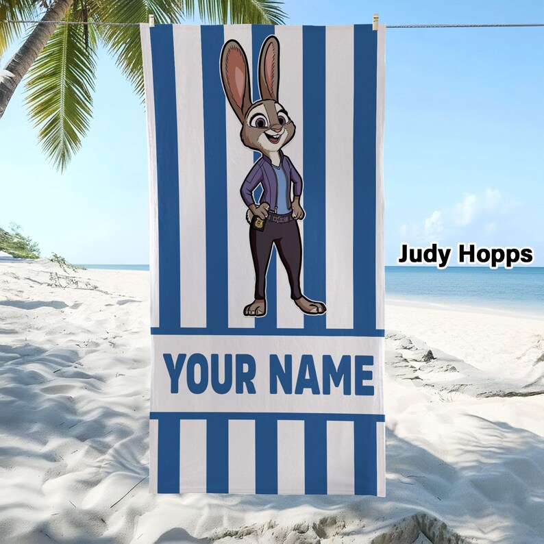 Puede incluir: Una toalla de playa rectangular con rayas verticales azules y blancas. En el centro, un personaje de conejo llamado Judy Hopps aparece representado con una chaqueta morada y pantalones oscuros. Debajo del personaje, aparece el texto YOUR NAME.