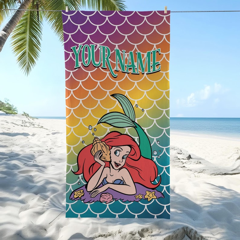 K&ouml;nnte beinhalten: Ein rechteckiges Strandtuch mit einem bunten Fischschuppenmuster in Regenbogenfarben. Der Text "YOUR NAME" ist oben in Gr&uuml;n aufgedruckt. Eine Zeichentrick-Meerjungfrau mit langem rotem Haar h&auml;lt eine beige Muschel an ihr Ohr, umgeben von Blasen.