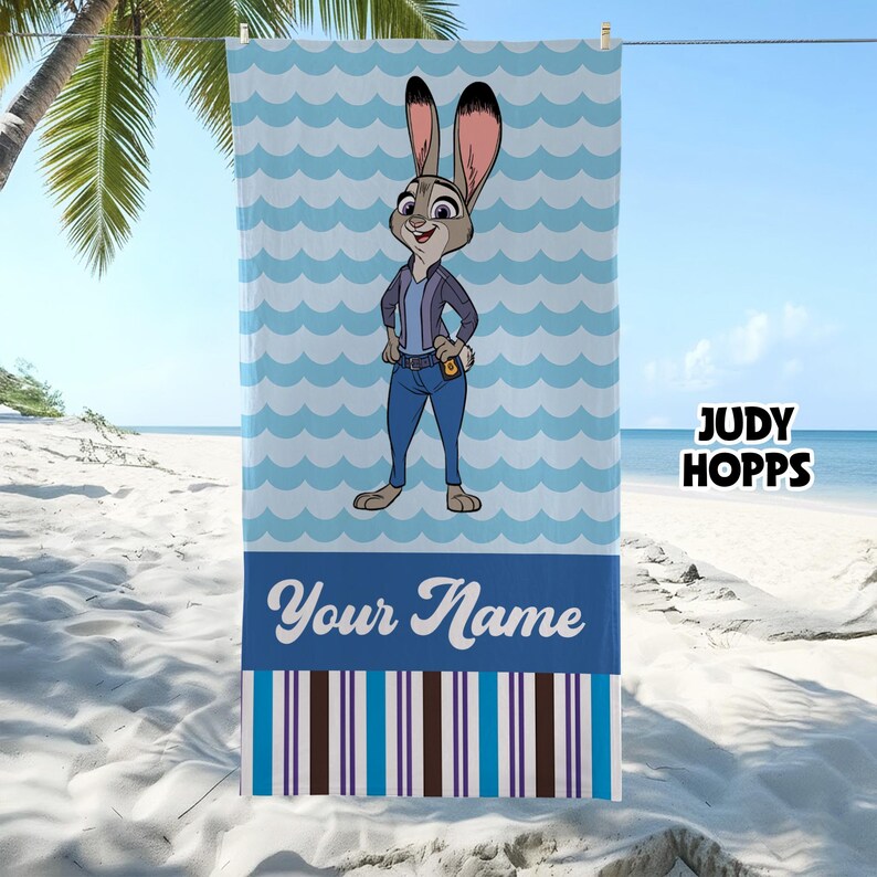 May include: A rectangular beach towel featuring a cartoon rabbit character wearing a jacket and jeans, centred against a light blue wavy pattern. The lower section displays the text Your Name above a series of vertical blue, white, and brown stripes.