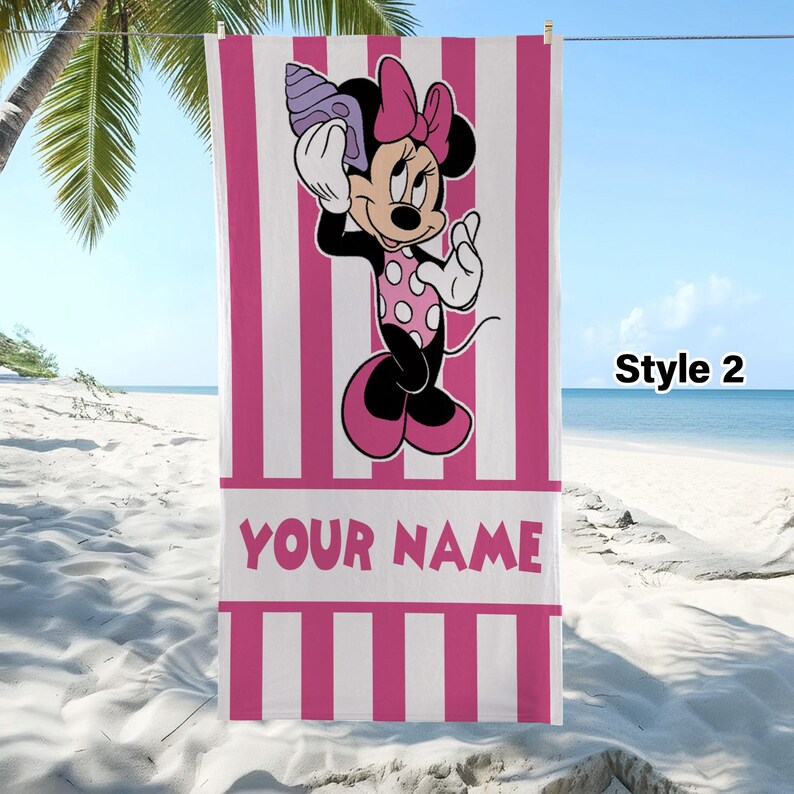 Pode incluir: Uma toalha de praia retangular com riscas verticais cor-de-rosa e brancas. O centro apresenta um gr&aacute;fico da Minnie Mouse a segurar uma concha junto ao ouvido. Abaixo da personagem, uma faixa horizontal branca cont&eacute;m o texto YOUR NAME.