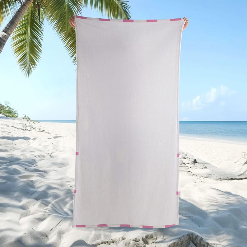 May include: A rectangular white beach towel featuring a border with a repeating pattern of small pink squares along the top, bottom, and side edges. The towel has a solid white center and a consistent fabric texture throughout the entire surface.