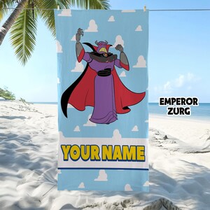 Op de afbeelding: Een rechthoekige strandhanddoek met een lichtblauwe achtergrond en witte wolken. Het personage Keizer Zurg staat in het midden afgebeeld, gekleed in een paars gewaad met een rode cape. Onder het figuur staat de tekst EMPEROR ZURG en YOUR NAME.