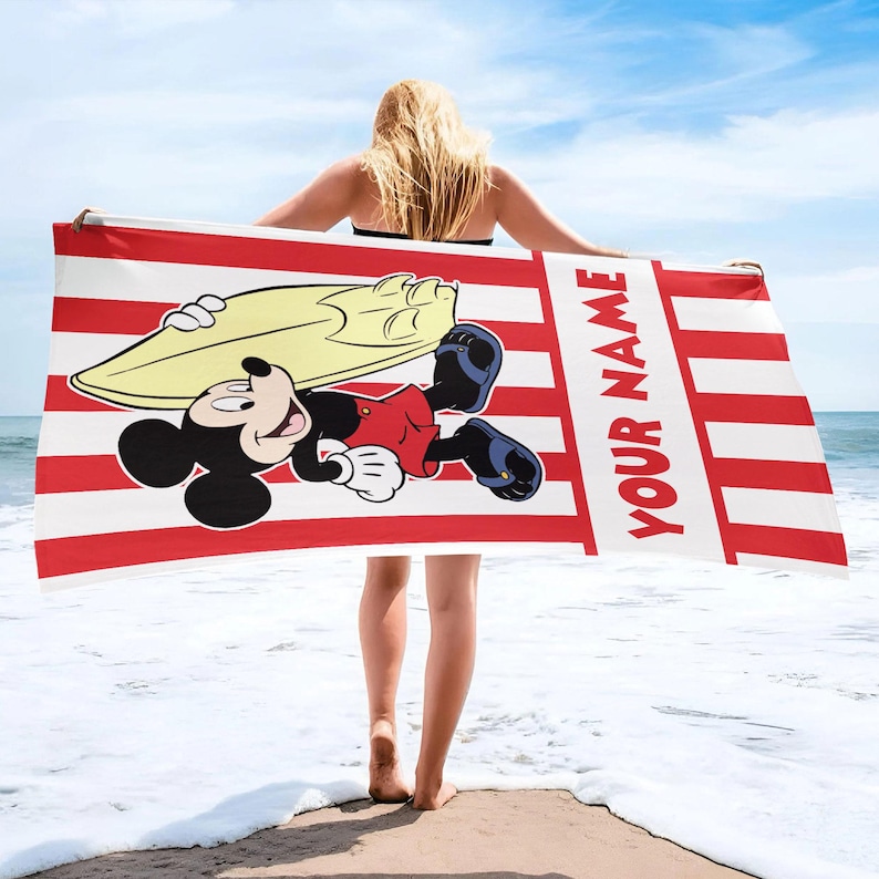 May include: A rectangular beach towel featuring a red and white vertical striped pattern. The towel displays a graphic of Mickey Mouse carrying a yellow surfboard, along with the text YOUR NAME printed vertically in bold red capital letters.