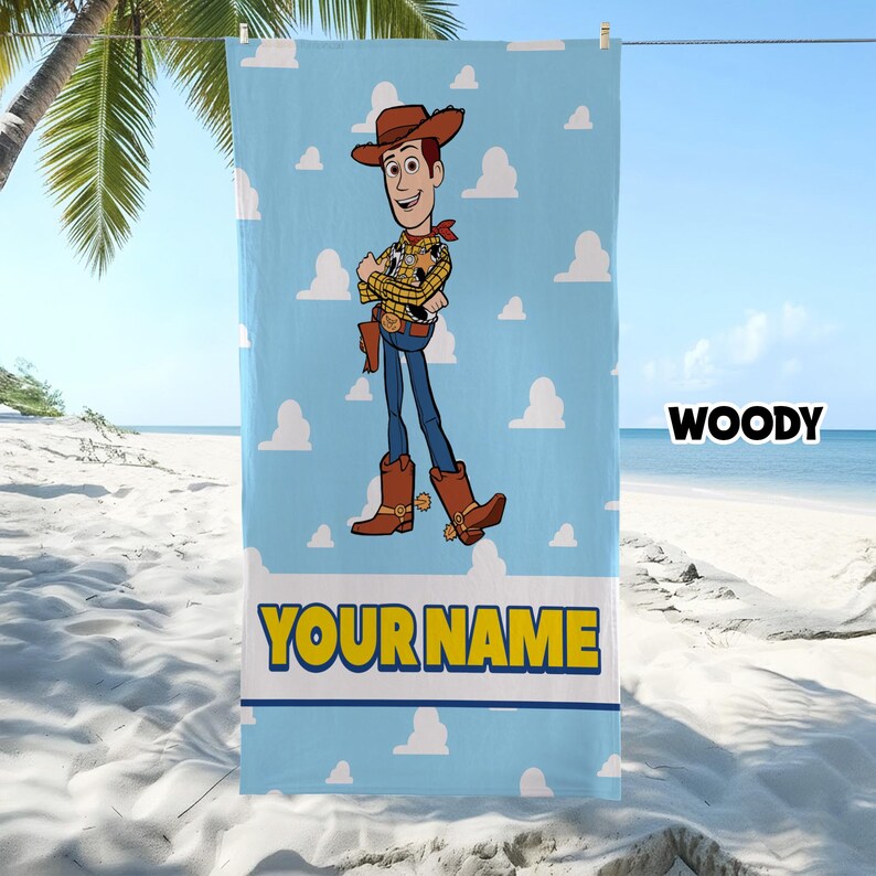 Puede incluir: Una toalla de playa rectangular con fondo azul claro y un patr&oacute;n de nubes blancas. El personaje Woody de Toy Story est&aacute; centrado, con sombrero de vaquero, camisa amarilla y vaqueros azules. El texto YOUR NAME aparece en color amarillo.