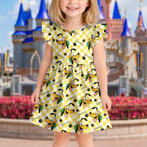 Könnte beinhalten: Gelb-weiß kariertes Kleid mit sich wiederholendem Muster von Pluto, Hundeknochen und Pfotenabdrücken. Das Kleid hat Rüschenärmel und wird von einem kleinen Kind getragen. Im Hintergrund ist ein Schloss zu sehen.