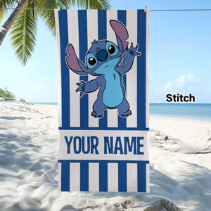 May include: A rectangular beach towel featuring a vertical blue and white striped pattern. The center displays a blue cartoon character with large ears and a light blue chest. Below the character is a white horizontal band with the text YOUR NAME.