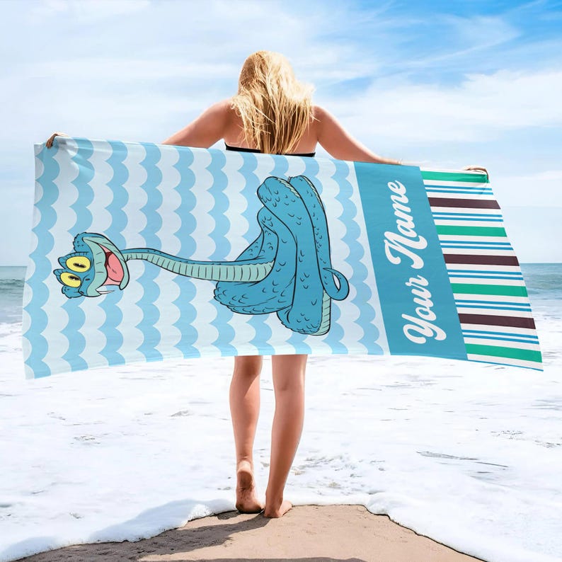 May include: A rectangular beach towel featuring a light blue and white wavy pattern background with a cartoon blue snake illustration. The towel includes a vertical blue section with the text Your Name and a multi-coloured striped border design.