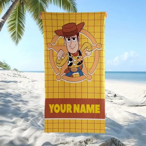 May include: A rectangular beach towel featuring a yellow grid pattern background with a central graphic of the character Woody from Toy Story wearing a brown cowboy hat, yellow shirt, and vest, positioned over a sheriff star, with the text YOUR NAME.