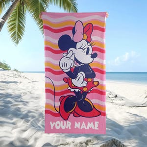 May include: A rectangular beach towel featuring a graphic of Minnie Mouse wearing a red polka-dot skirt and a pink bow. The background consists of horizontal wavy stripes in shades of pink, orange, and red. The text YOUR NAME is printed in white.