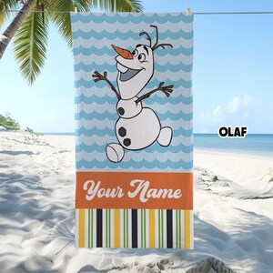May include: A rectangular beach towel featuring a cartoon snowman with a carrot nose and twig arms centered on a light blue wavy background. Below the character is an orange horizontal band with the text Your Name and a striped pattern.