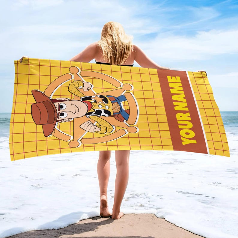May include: A rectangular beach towel featuring a yellow grid pattern background with a central graphic of a cartoon cowboy character wearing a brown hat and a sheriff badge. A brown vertical stripe on the right side contains the text YOUR NAME.