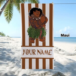 May include: A rectangular beach towel featuring vertical brown and white stripes. The center displays a cartoon character with dark curly hair, tribal tattoos, and a green leaf skirt. Below the character, the text reads YOUR NAME in brown letters.