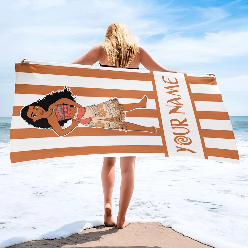May include: A rectangular beach towel featuring a pattern of vertical white and tan stripes. The towel displays a cartoon illustration of a character with long dark hair wearing a patterned top and skirt, with the text YOUR NAME printed vertically.