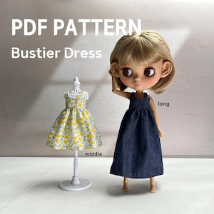 May include: A PDF pattern for a bustier dress featuring a doll wearing a long dark blue denim dress and a miniature mannequin displaying a middle-length dress with a yellow lemon print on a white background. The text reads PDF PATTERN Bustier Dress.